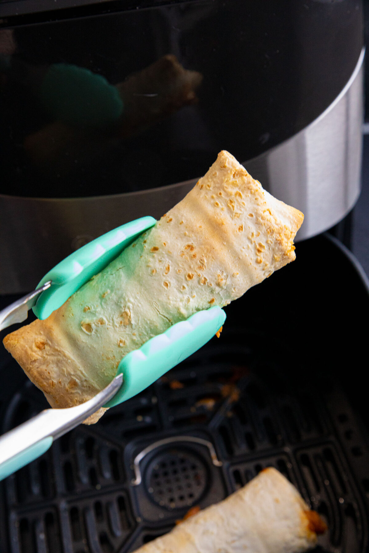 cooked burritos held by a pair of tongs
