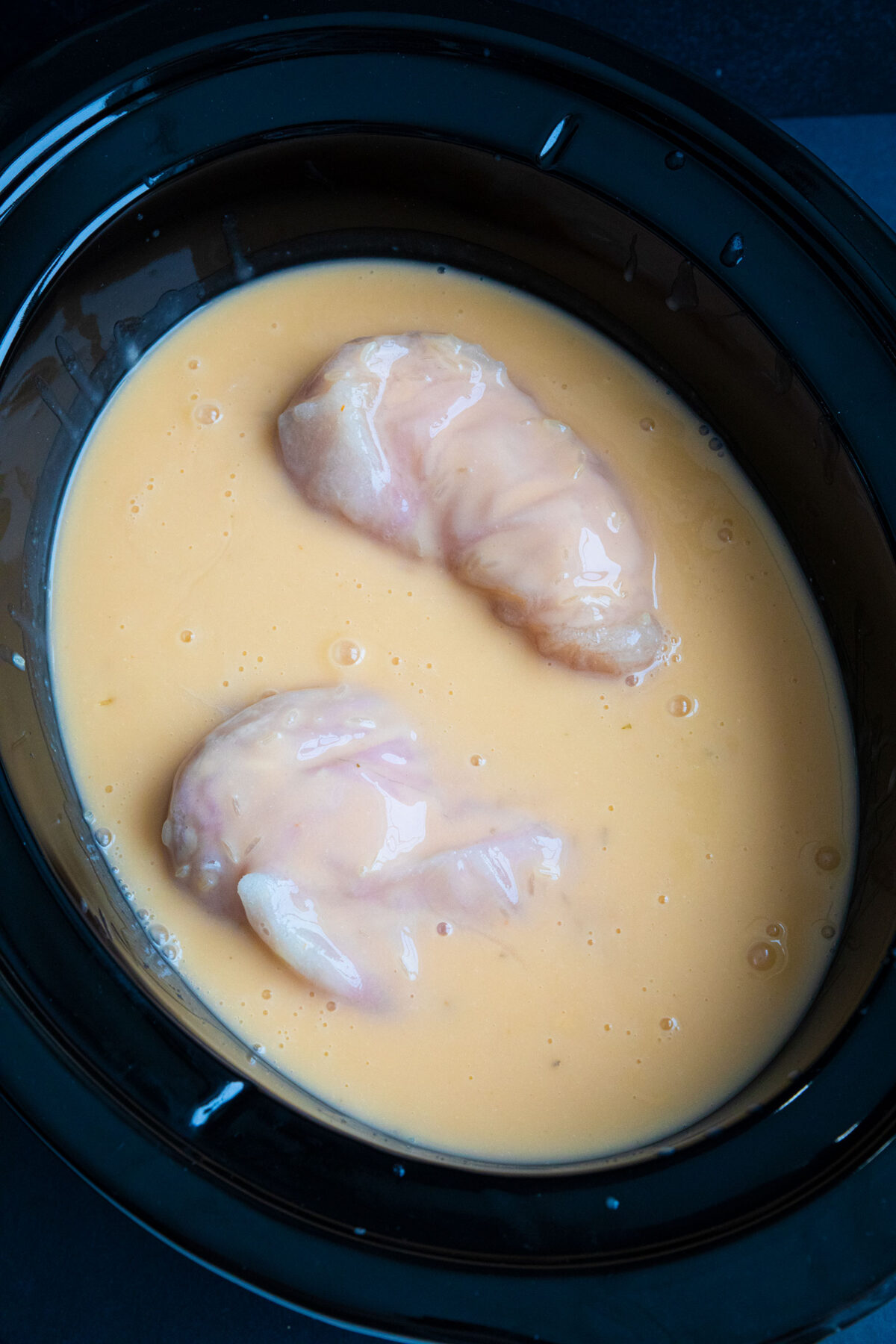 rice and cheese sauce poured on top of chicken breasts in slow cooker