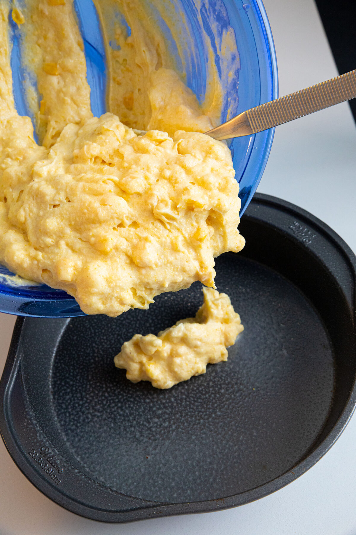spooning out cornbread batter into a prepared pan 