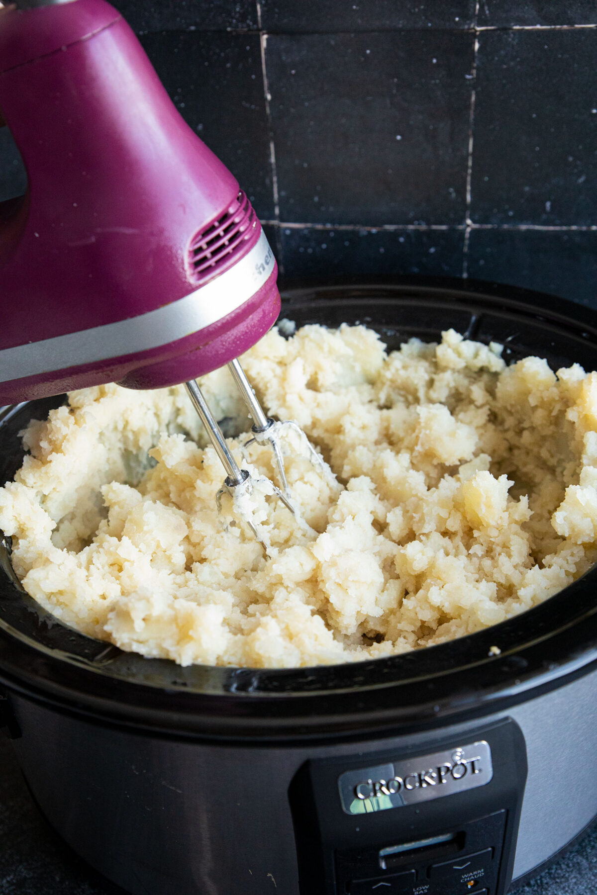 using a hand mixer to beat potatoes in a slow cooker 
