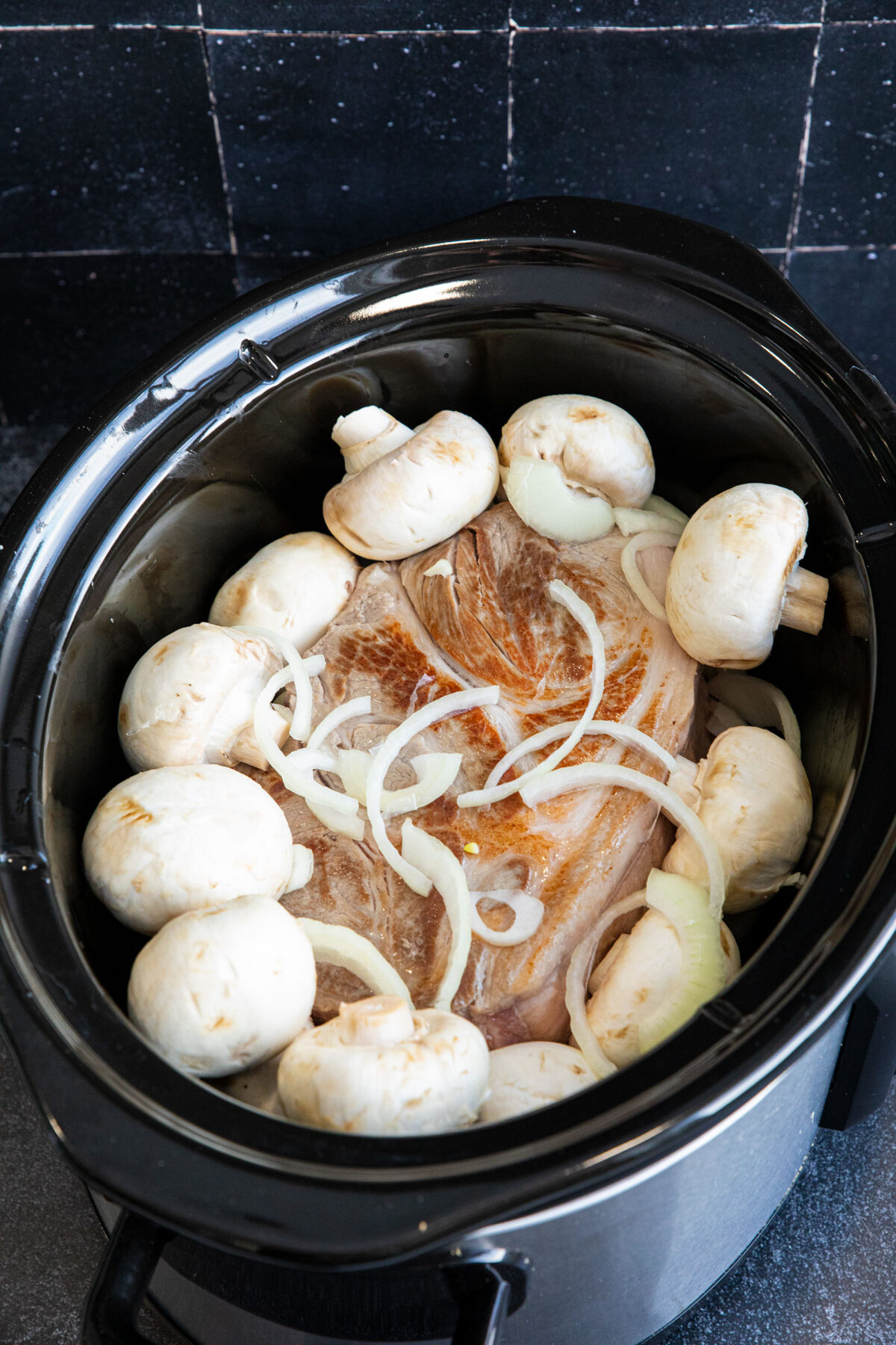 browned pork roast in slow cooker with onions and mushrooms on top 