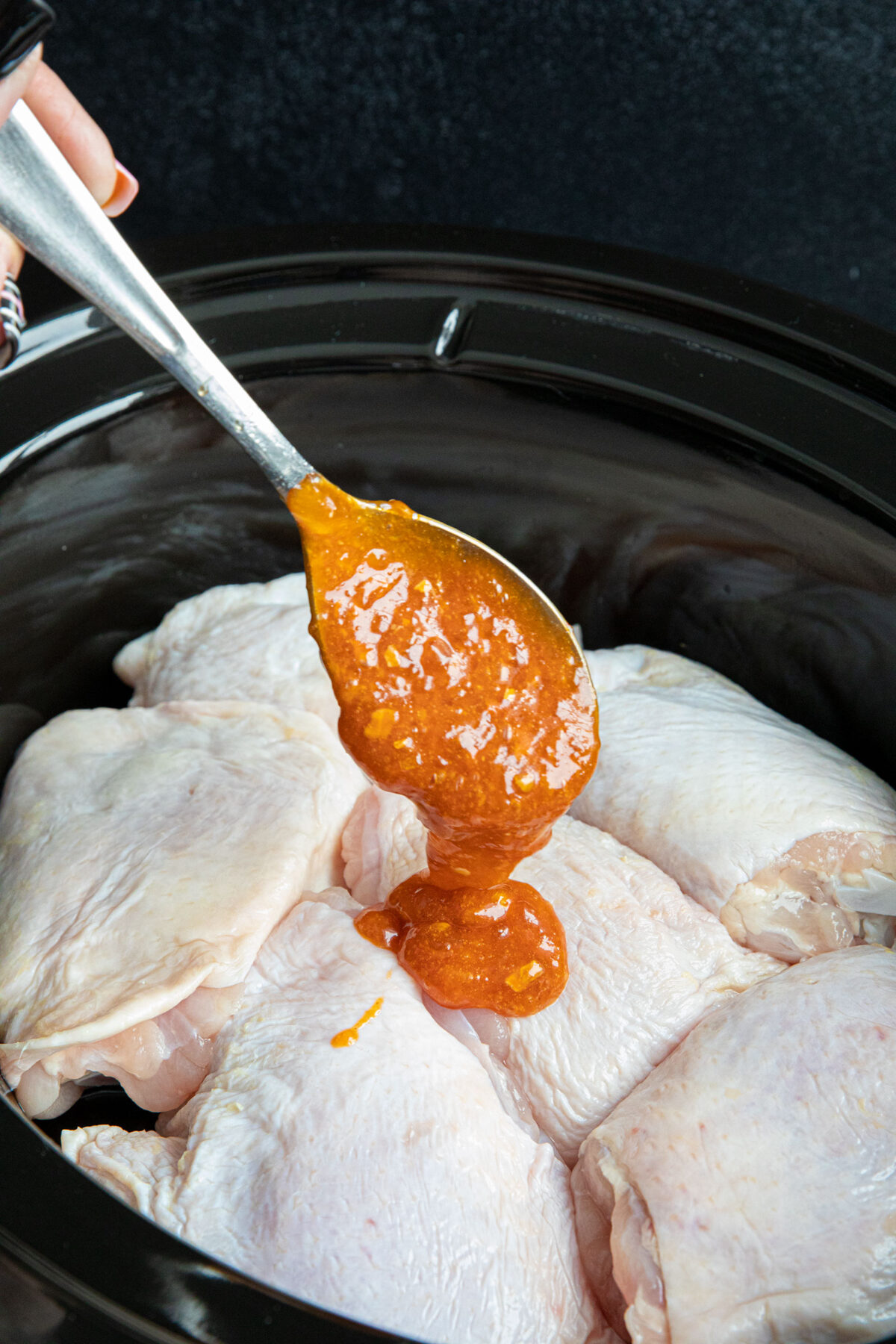 spooning apricot sauce over chicken thighs in the slow cooker 