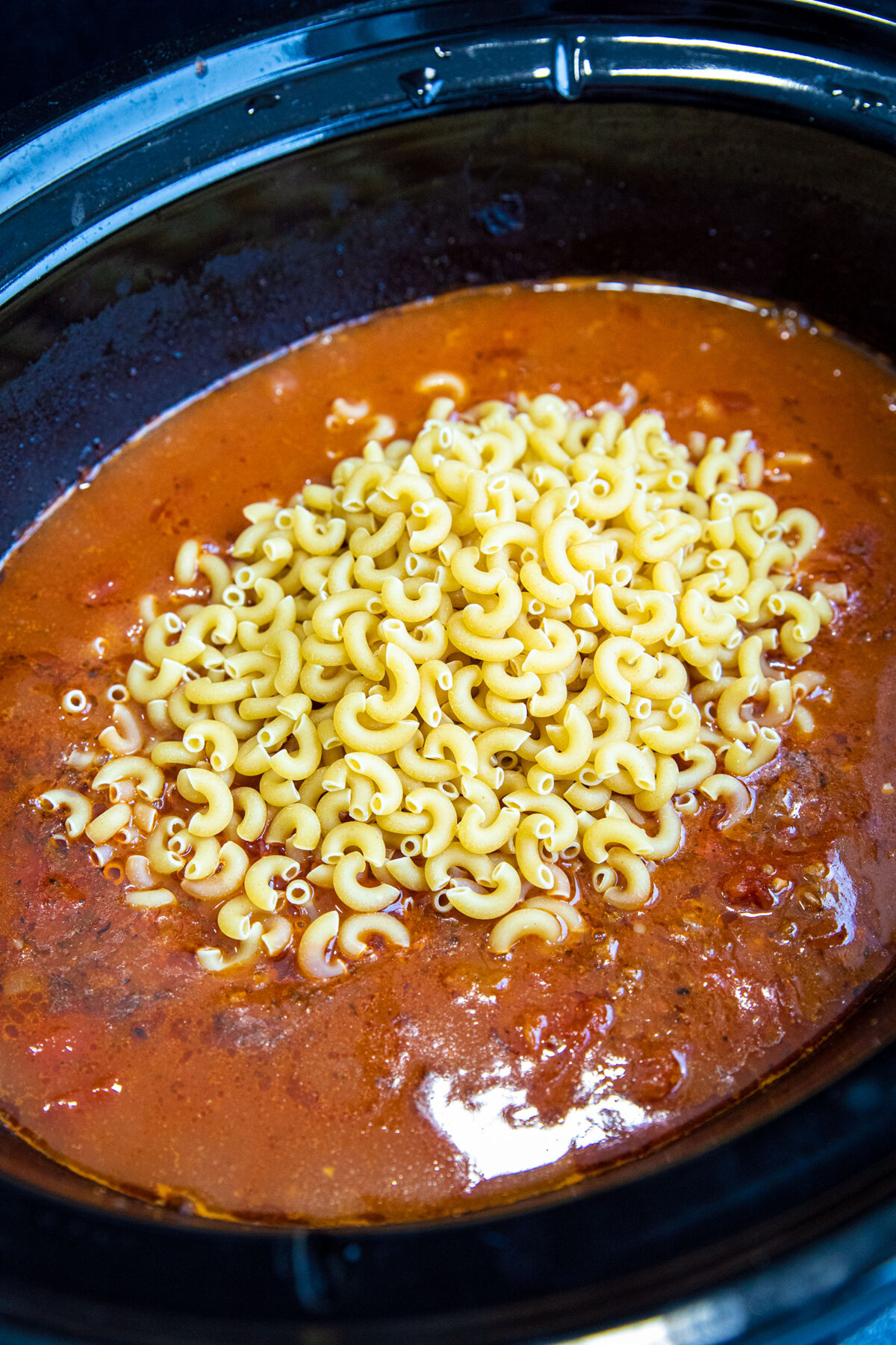 uncooked elbow macaroni being added to slumgullion 