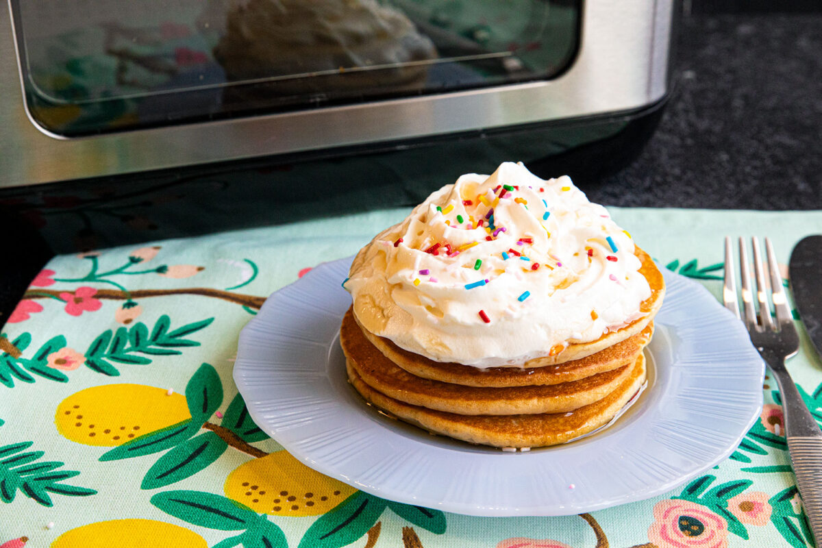 air fryer cooked pancakes on a plate with whipped cream and sprinkles