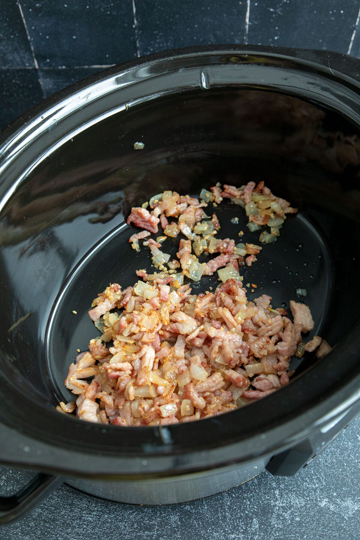 bacon and onions in the bottom of a black slow cooker